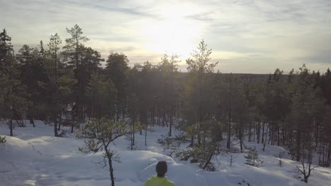 winter hiking man on mountain top in ice cold arctic forest watching sunset view