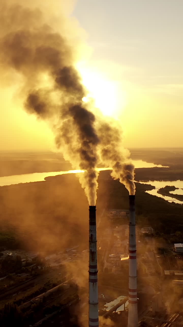 Dirty emissions coming out of industrial pipes. Factory surrounded by nature in the evening. Thick smoke going into th air from manufacturing at sunset. Pollution. Vertical video