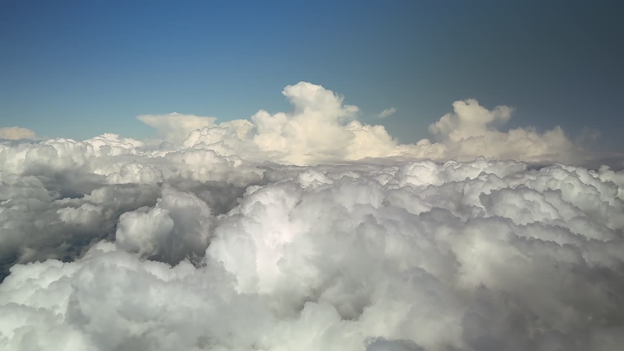 An aerial POV stormy cloudscape taken from an airplane cockpit while flying at high altitude in a blue sky plenty of cottony and towering storm clouds bathed by the sunset light. Ultra-realistic 4K