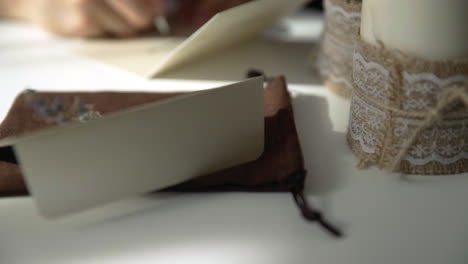 Schöne-Weibliche-Hand,-Die-Eine-Hochzeits--Oder-Feiertagseinladung-Auf-Einem-Hellen-Weißen-Tisch-Mit-Kerzen-Schreibt