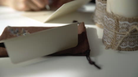 Beautiful-female-hand-writing-a-wedding-or-holiday-invitation-on-a-bright-white-table-with-candles