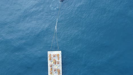 floating barge with construction equipment being towed through the ocean by a tugboat