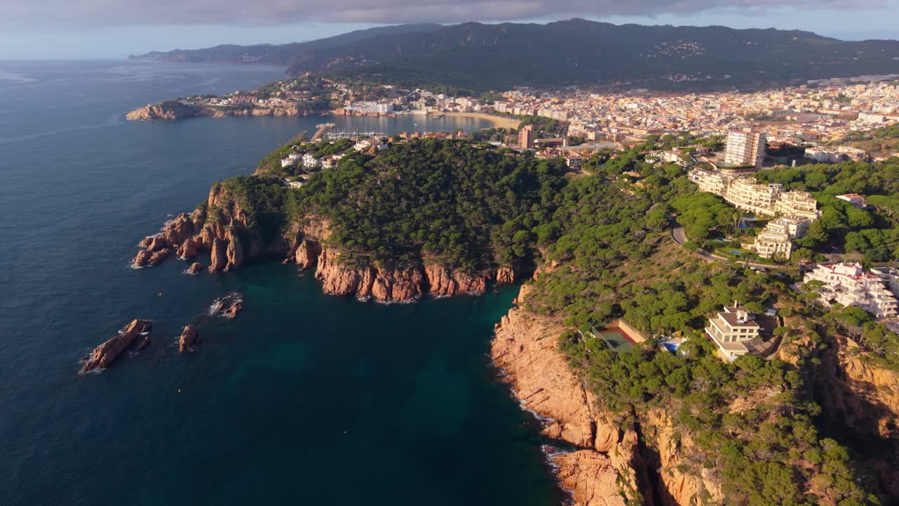Fantastisk luftperspektiv, der viser den klippefyldte kystlinje og smukke by Sant Feliu de Guíxols i Costa Brava, Spanien, med Middelhavet og frodige, grønne klipper ved solnedgang