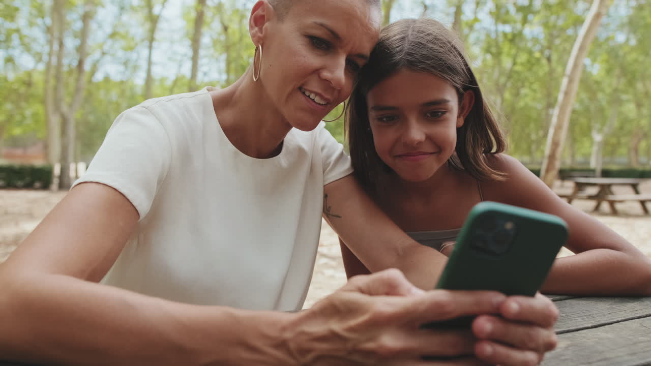 Happy Mother and Daughter Looking at Smartphone Together in Park