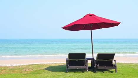 two empty chaise lounge chairs sitting under a shade umbrella facing the incoming tide