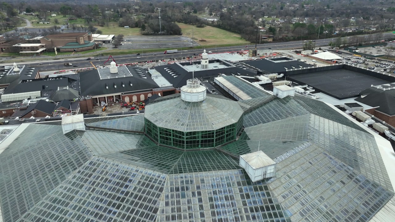Aerial flyover Nashville Opryland Convention Center showing glass roof structure, surrounded by busy highways, nearby buildings and light traffic. Large-scale urban architecture in Tennessee, USA.