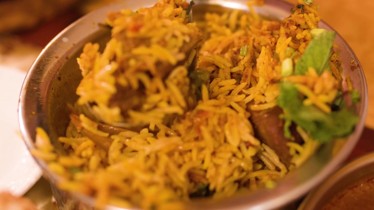 Primer plano de una cuchara sirviendo arroz basmati aromático y pollo de un tazón de metal tradicional.
