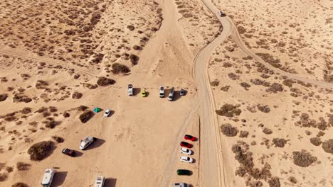 forward tilt up drone view of a coastal parking area with cars and motorhomes in fuerteventura, near a volcanic beach. shot at sunset with golden tones, evoking travel spirit and warm tranquility