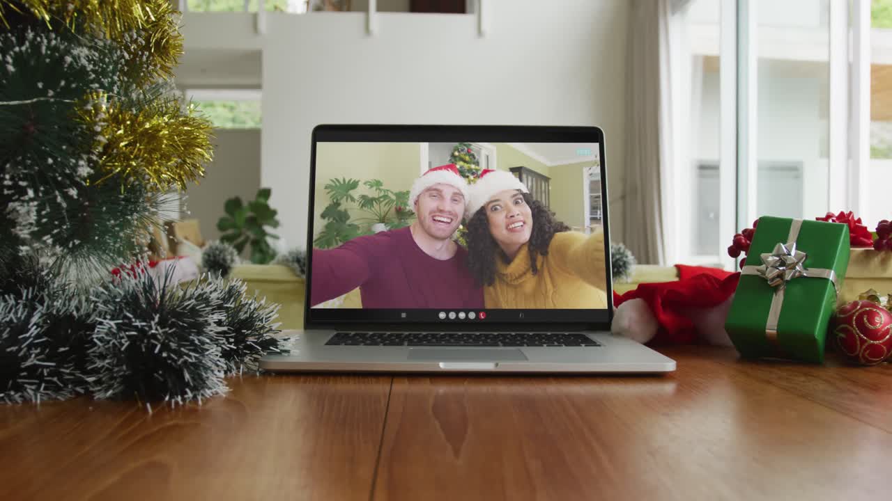 una pareja diversa sonriente con sombreros de santa claus en una videollamada de navidad en una computadora portátil