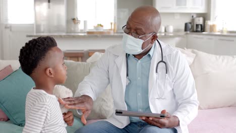 Senior-african-american-male-doctor-in-face-mask-using-tablet-with-boy-patient-slow-motion