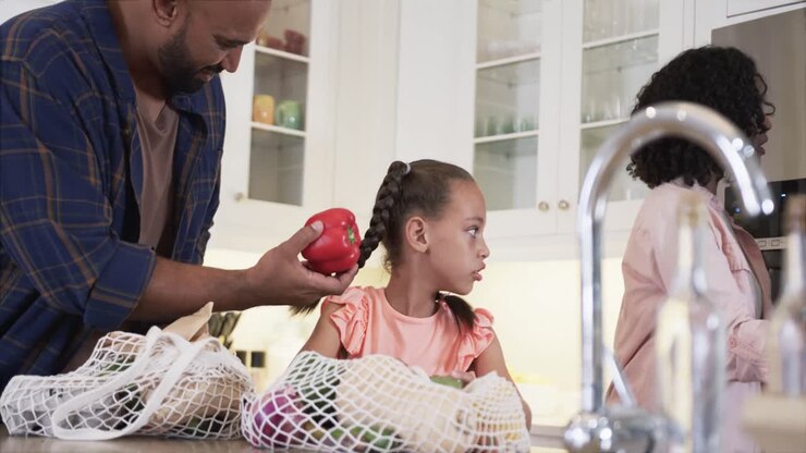 Happy biracial father, mother and daughter unpacking shopping in kitchen, slow motion