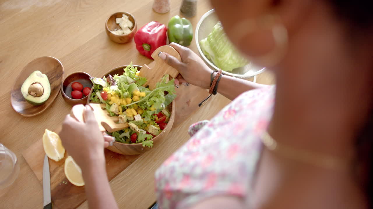 Preparing fresh salad, woman mixing vegetables in wooden bowl in kitchen