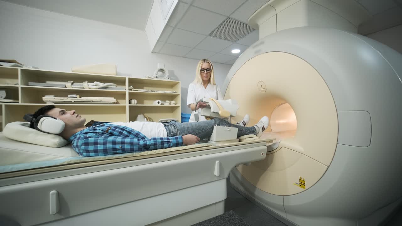 mujer médico hace escaneo de resonancia magnética de la articulación de la rodilla. joven paciente en la mesa automática entra en una máquina de resonancia eléctrica de tipo cerrado usando auriculares de aislamiento de ruido. equipo moderno, bobina en la rodilla del paciente