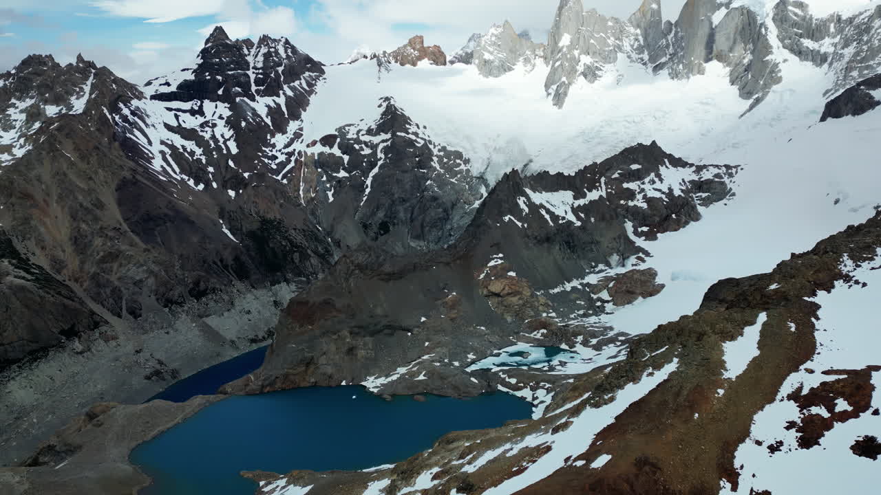 Aerial drone view of a bright turquoise glacial lake nestled between steep rocky cliffs and snow covered peaks