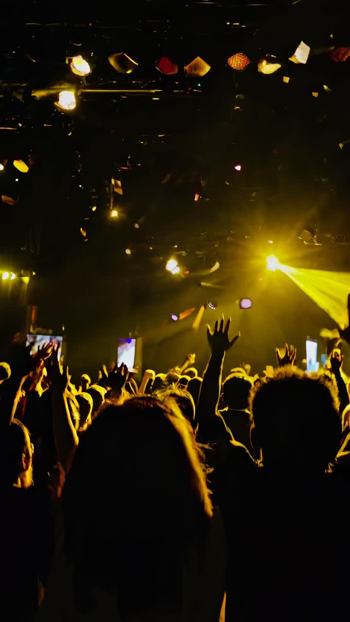 Vibrant video of a concert scene with colorful lights and raised hands, captured from a low-angle