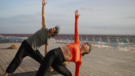 couple practicing yoga on a pier by the sea