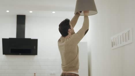 hombre blanco apagando la lámpara de araña en la cocina. joven girando la bombilla