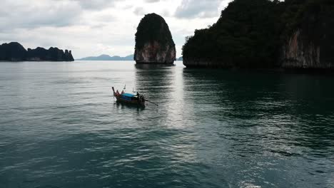 drone footage of longtail boat navigating around islands of thailand with the limestone rock formations sticking out of the water and the ocean in background-5