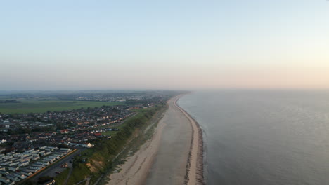 Toma-Aérea-De-Drones-Volando-A-Lo-Largo-De-Una-Larga-Playa-Vacía-De-Arena-Con-Tierra-Plana-Cubierta-De-Hierba-En-La-Costa-De-Norfolk-En-Gran-Bretaña-Al-Atardecer