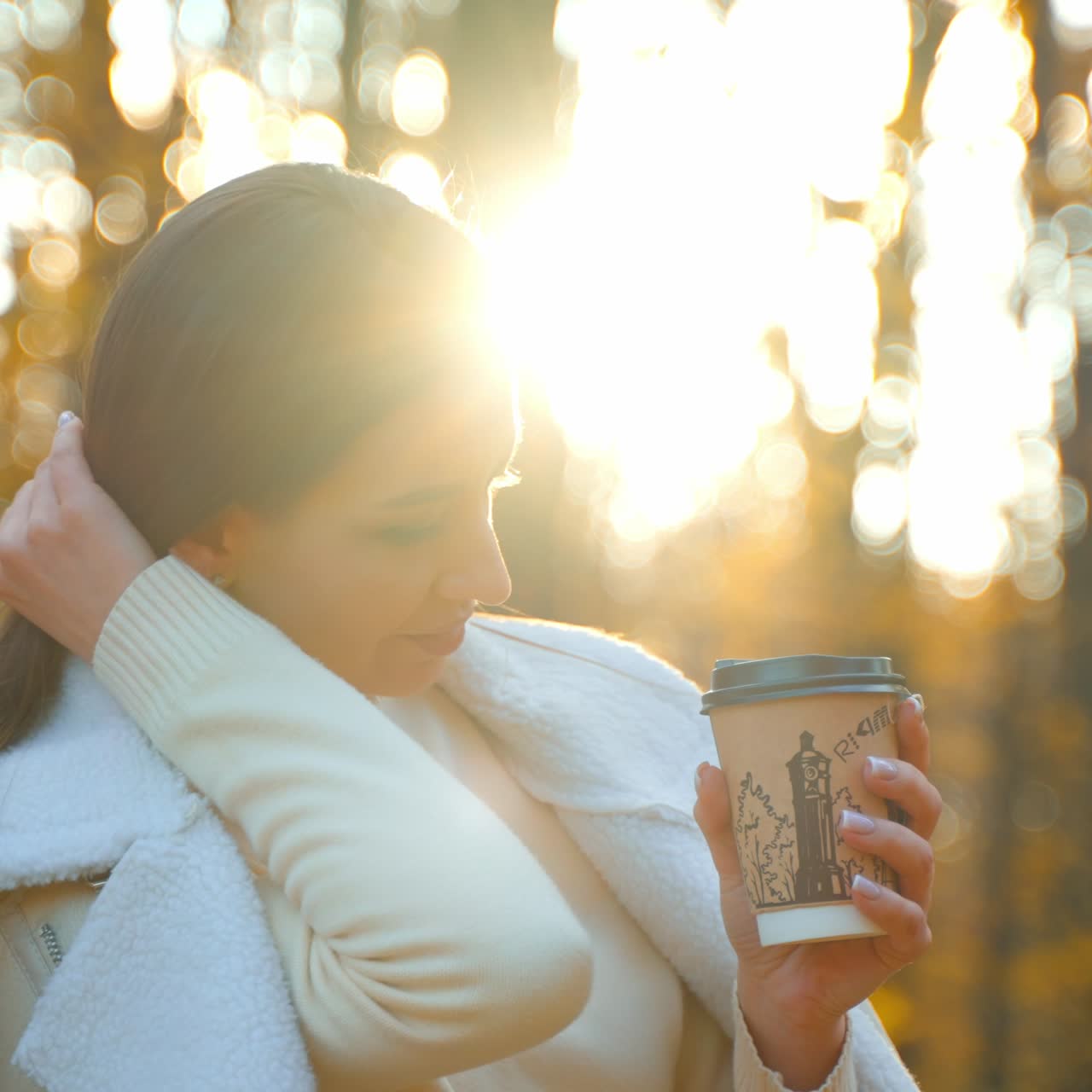 Attractive brunette lady holding a paper cup in her hands. Woman is having a walk in the nature in autumn season