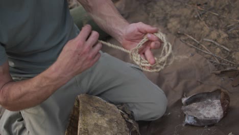 caucasian male survivalist preparing tinder from twine to make fire at camp in wilderness