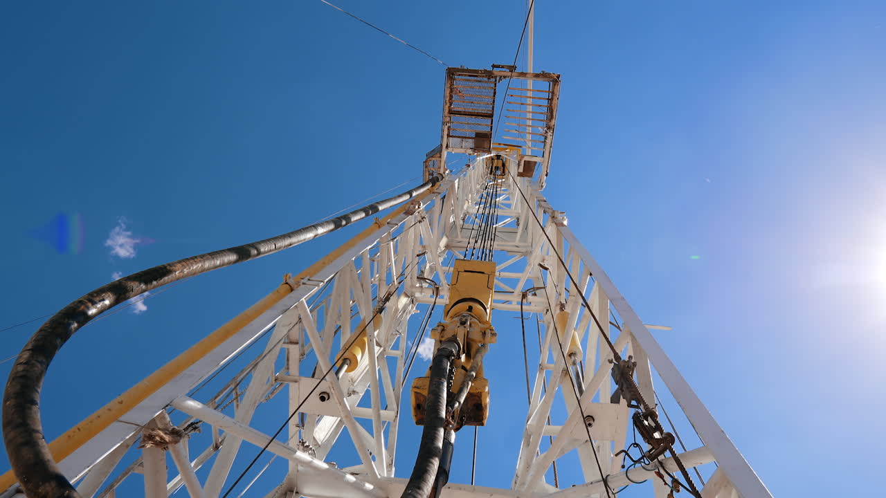 Working boer attached to the high metal derrick. Equipment at the oil production industry. Low angle view.