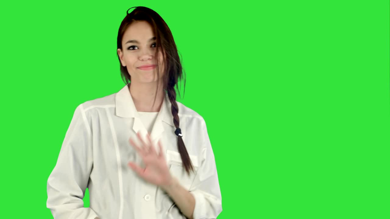실험실 코트에 미소 짓는 젊은 여성이 녹색 화면에서 재미있는 춤을 추고, 크로마 키