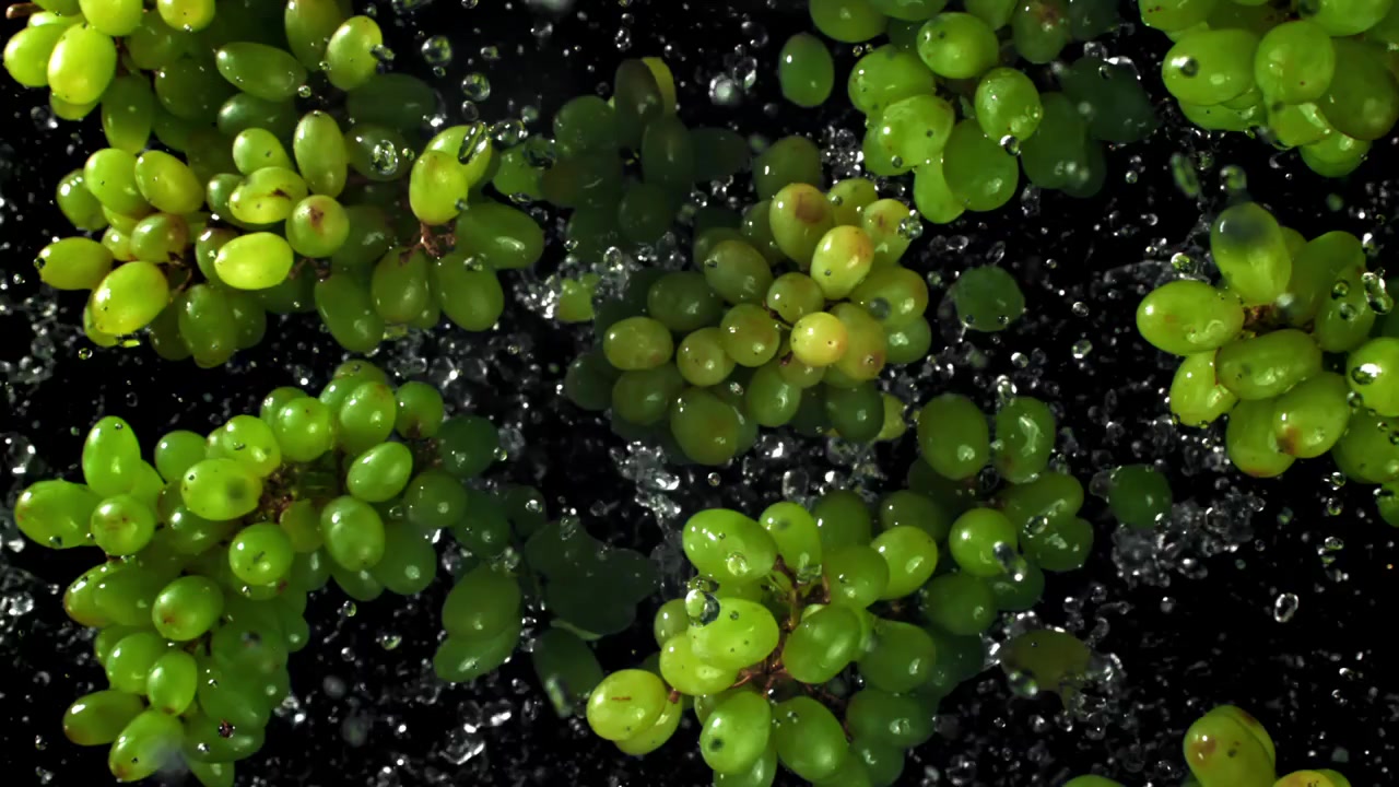 Uva verde fresca con schizzi d'acqua su sfondo nero