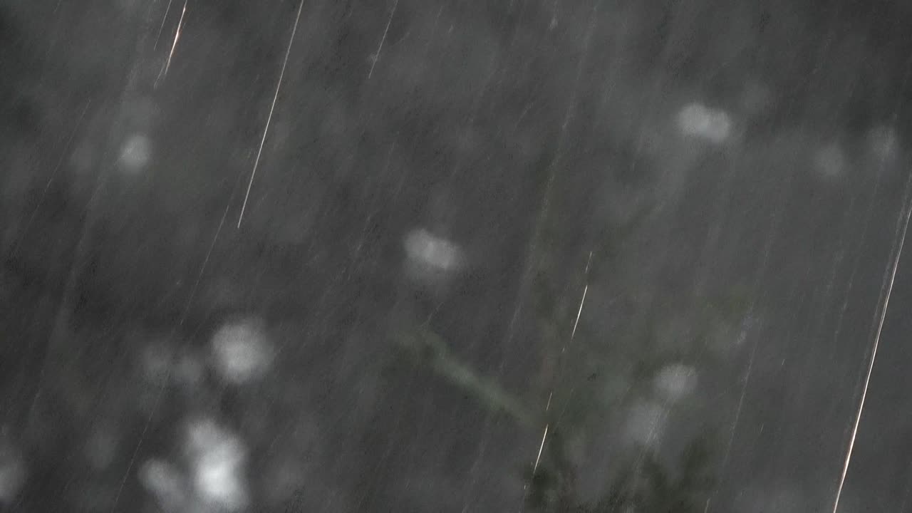 Dense rainshield, fast falling raindrops with motion blur, against an unclear grey background