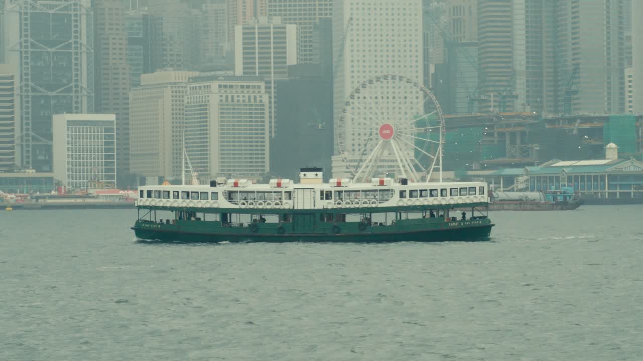 霞がかったヴィクトリア・ハーバーを横断するスターフェリー。背景には香港のスカイラインと観覧車が見える。
