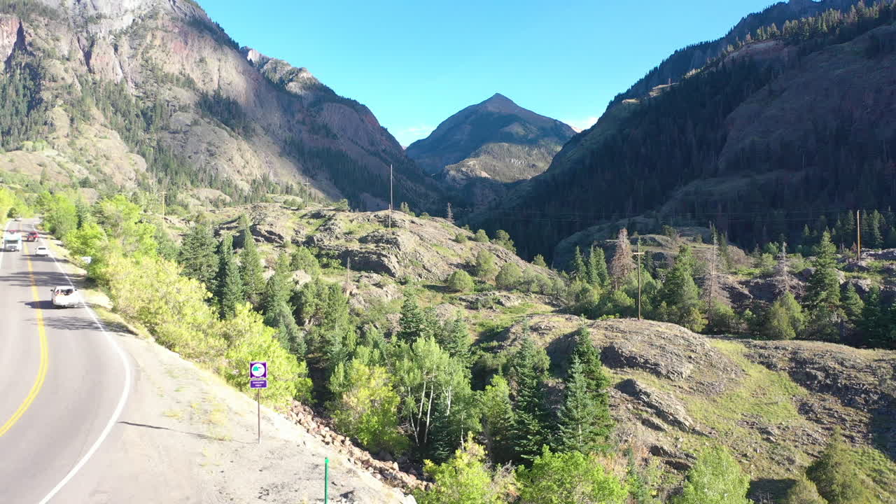 drone aéreo levantando el movimiento de los autos que conducen con portaequipajes en la autopista 550 a través de las montañas ouray colorado rodeadas por un espeso bosque de pinos y líneas eléctricas