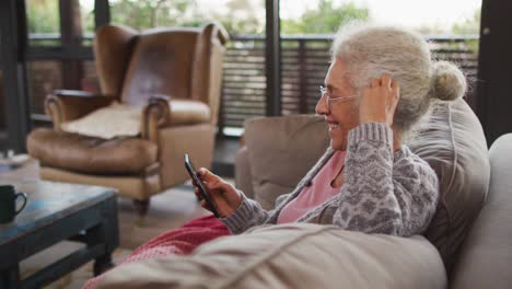 senior mixed race woman sitting on sofa using smartphone