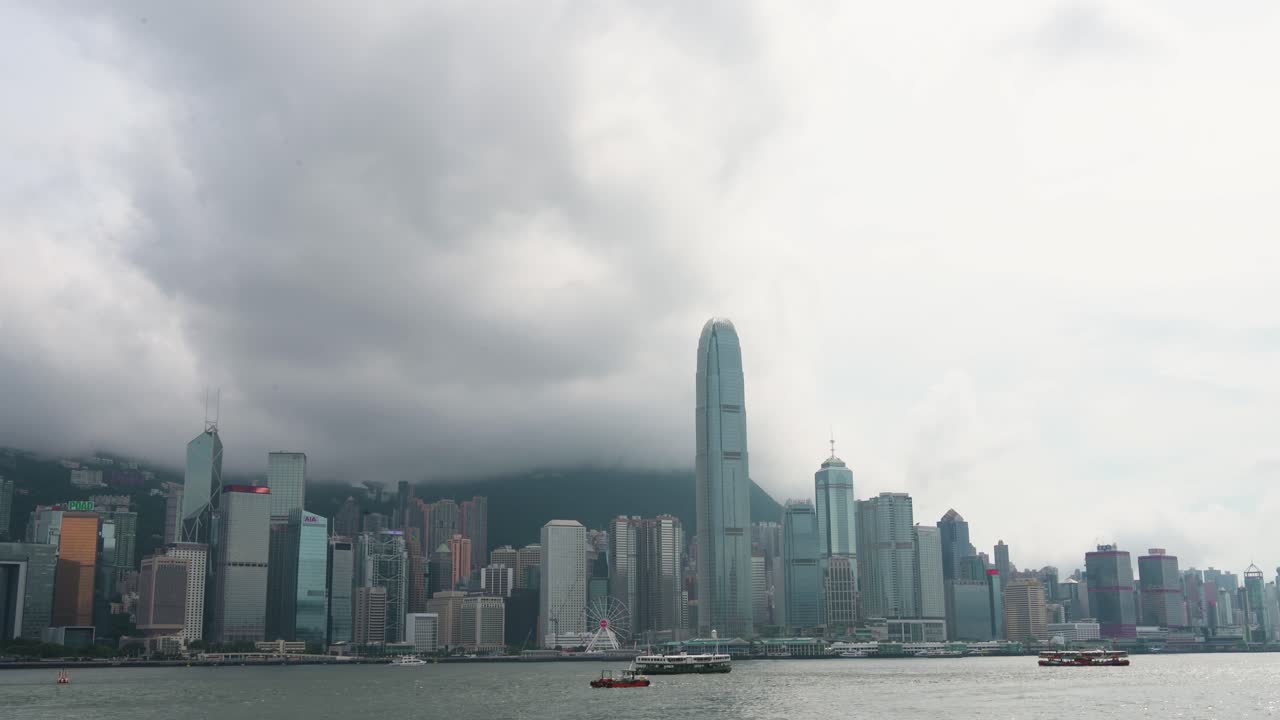 Ferries and boats sail across Victoria Harbour on a cloudy day, with the iconic Hong Kong Island financial district skyline as backdrop in Hong Kong, China.