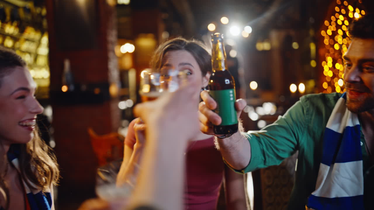 Primo piano di studenti entusiasti che esultano a una partita in un pub moderno mentre bevono birra