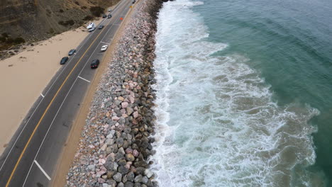 pacific ocean waves crashing on california shore, aerial drone shot over moving traffic