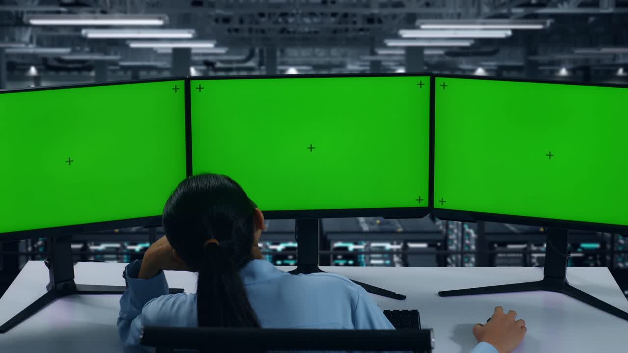 데이터 센터에서 여러 컴퓨터 모니터를 모방하는 지루한 아시아 여성의 뒷면
