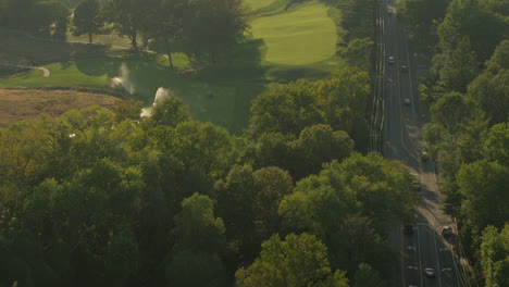 Flyover-a-golf-course-and-nearby-road-at-sunset-with-sprinklers-running