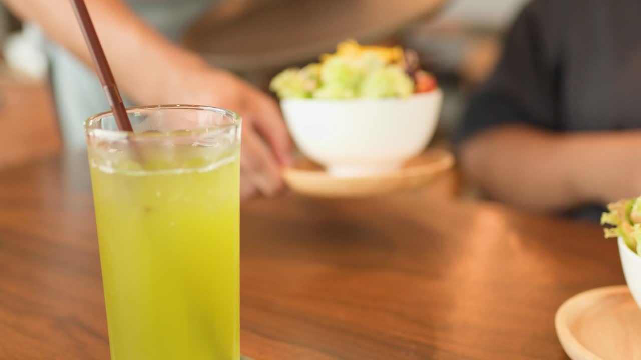 Server places fresh salad beside green tea for customer in bright, modern cafe setting