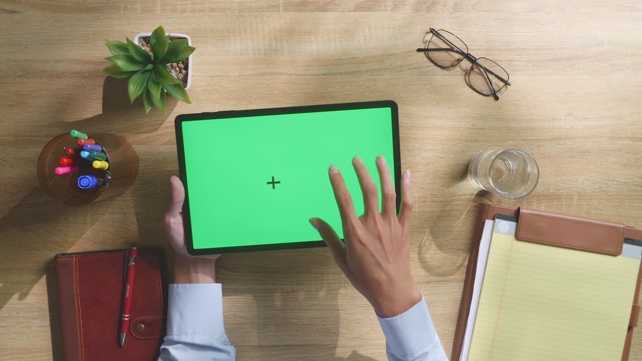 vista de arriba hacia abajo de una computadora portátil con pantalla verde simulada pantalla chromakey en un escritorio de oficina de madera al lado de la libreta con bolígrafos, gafas y un vaso de agua.