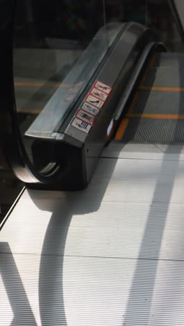 una vista detallada de una escalera mecánica que desciende en un centro comercial, capturada desde una perspectiva en primera persona utilizando una cámara portátil. la escena destaca la mecánica de la escalera mecánica