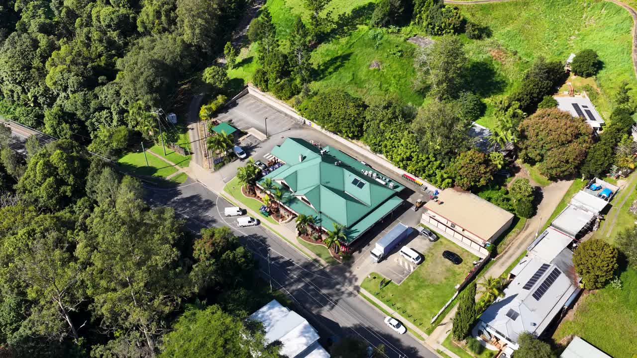Aerial footage captures a small rural town surrounded by lush greenery in Uki, NSW, under bright daylight