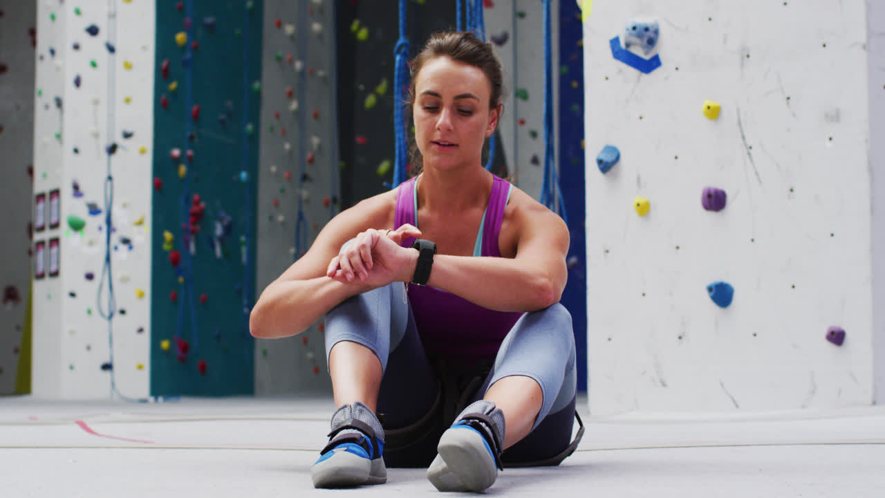 mujer caucásica comprobando su reloj inteligente preparándose para escalar en una pared de escalada interior