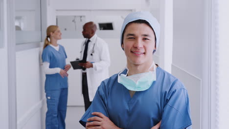 cirujano masculino con trajes y máscara de pie en el pasillo del hospital con colegas en el fondo