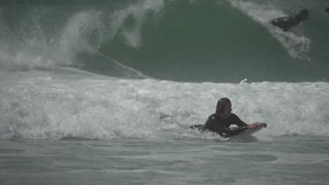 surfer in wetsuit paddles through foamy whitewater under overcast skies, pushing toward the lineup. realistic ocean action, endurance and focus