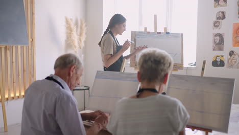 el maestro muestra a un grupo de amigos de personas jubiladas en los cursos de dibujo. un grupo de hombres y mujeres de edad avanzada dibujan juntos y sonríen