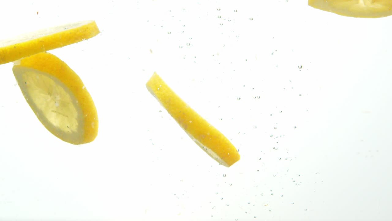Limone appena tagliato che cade nell'acqua, isolato su sfondo bianco