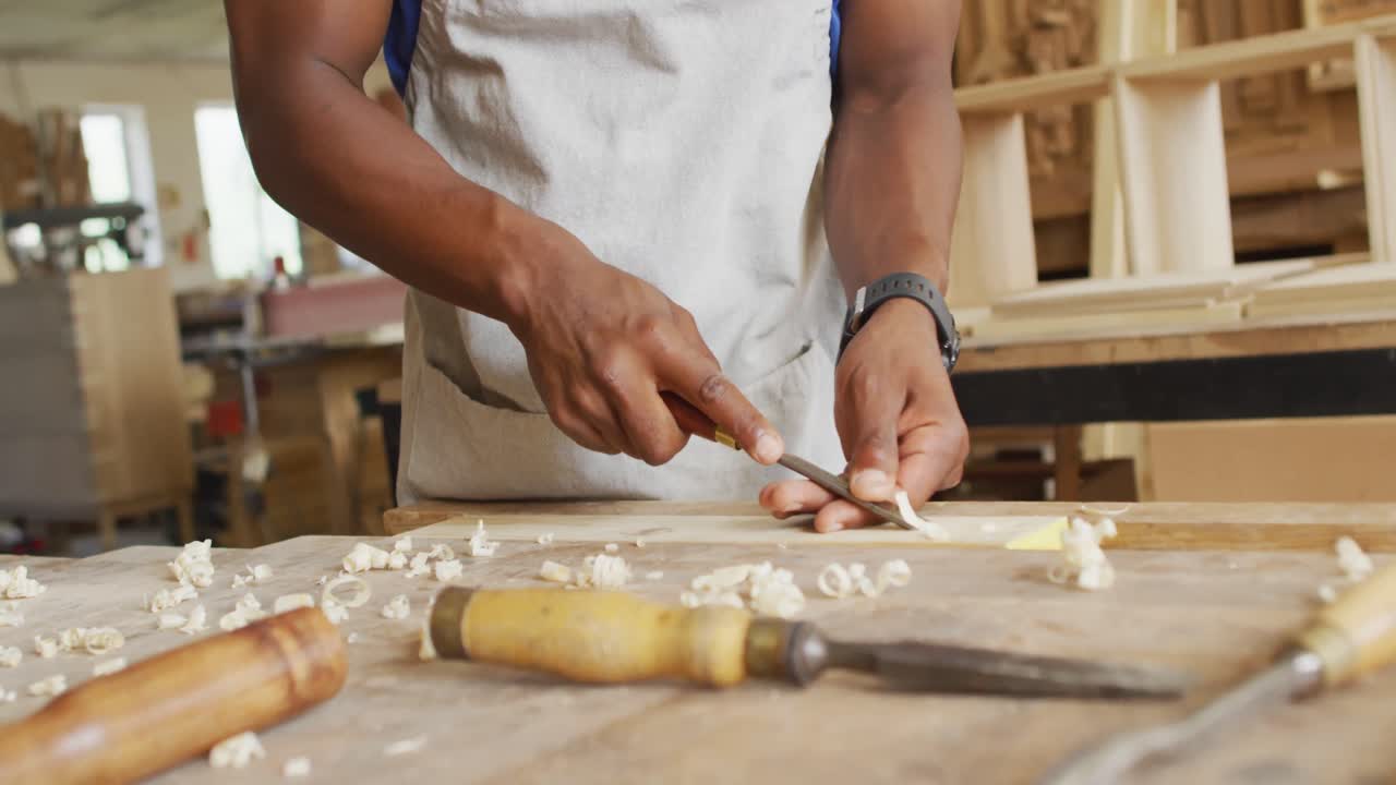 Mid section of african american male carpenter carving wood with chisel at carpentry shop