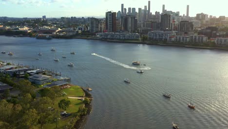 aerial view tilt up shot capturing newstead river terrace, waterfront residential apartment complex along brisbane river with downtown cityscape on the skyline at sunset, capital city of queensland