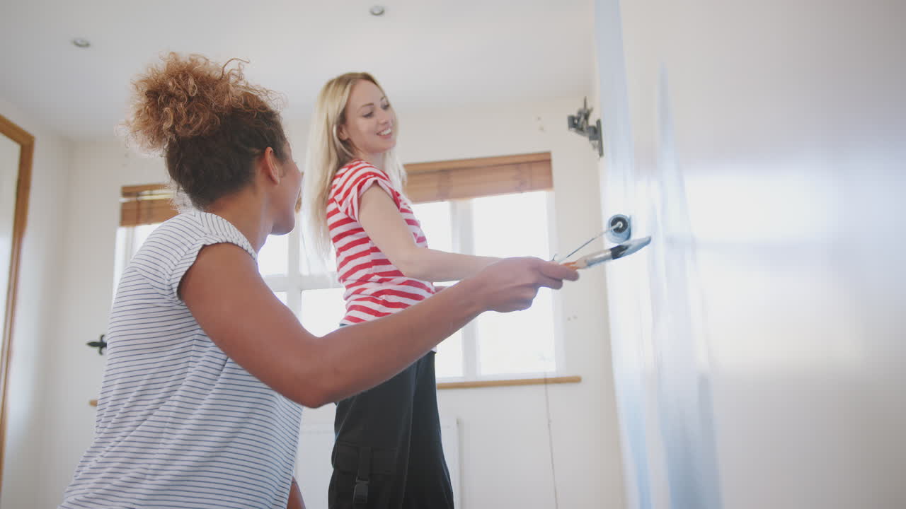 dos mujeres decorando una habitación en una nueva casa pintando la pared juntas