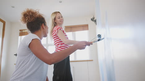 two women decorating room in new home painting wall together